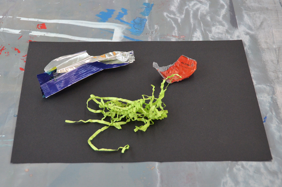Farbe als Gestaltungsmittel: Das Bild zeigt die drei als Mutterfarben gewählten Objekte in den Farben Rot, Grün, Blau - Zwei Verpackungen von Süssigkeiten und Papierschnippsel.