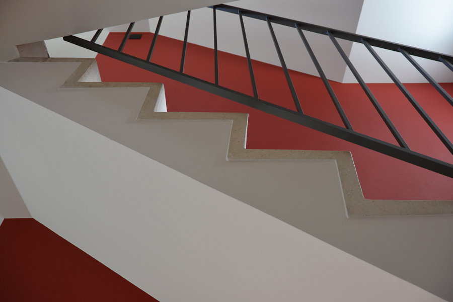 Farbgestaltung Innenraum: Das Bild zeigt eine Detailansicht im Treppenhaus zum Mittelgeschoss mit roter Akzentwand.