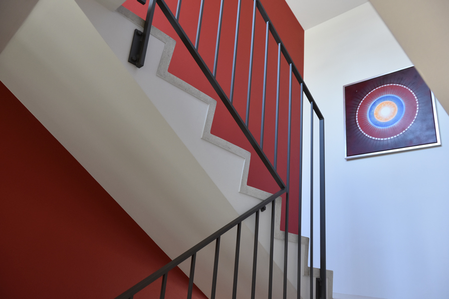 Farbgestaltung Innenraum: Die Detailansicht zeigt das Kontrastspiel im Treppenhaus zwischen der roten Akzentwand, dem schwarzen Metallgeländer und den hellen Tritten des Treppenhauses.