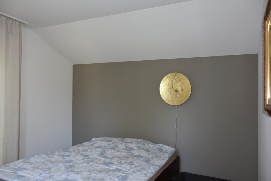 Farbgestaltung Innenraum: Das Bild zeigt das Schlafzimmer im Dachgeschoss mit Blick auf das Bett mit Rückwand als Akzent, die in mittleremn, erdigem Umbraton gestrichen ist.