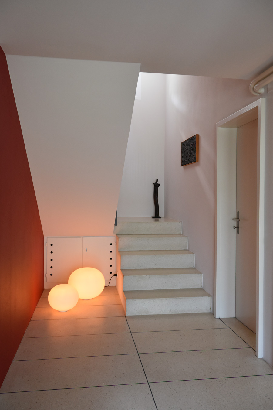 Farbgestaltung Innenraum: Das Bild zeigt den Eingangsraum des Hauses im Strassengeschoss mit dem Blick auf das Treppenhaus zum Mittelgeschoss und der seitlichen roten Akzentfarbe.
