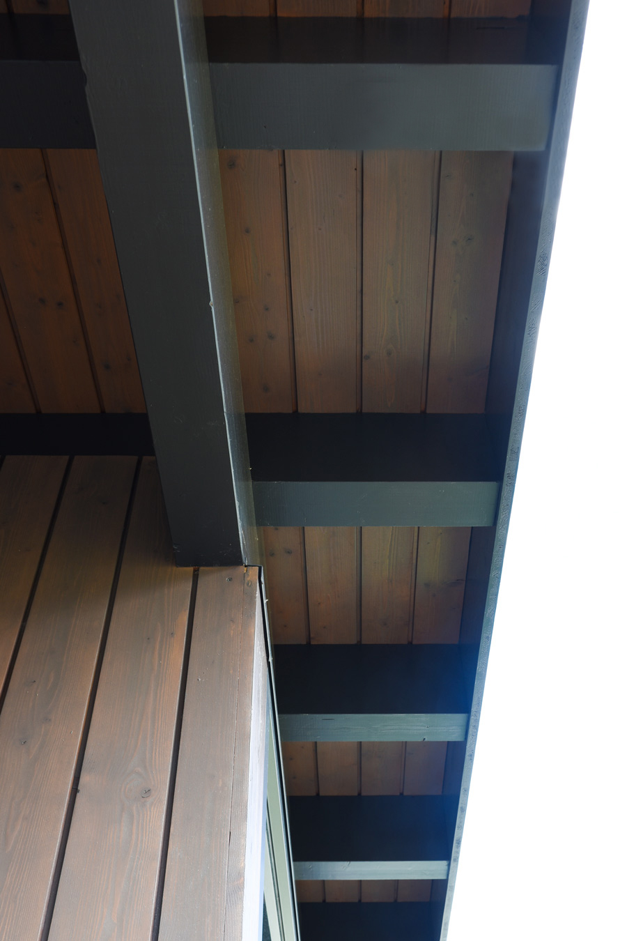 Farbgestaltung Holzfassade: Das Bild zeigt die Untersicht des Vordaches auf der Nordseite des Atelieranbaus mit dem Helldunkelkontrast zwischen Tragelementen und Holzverschalung.