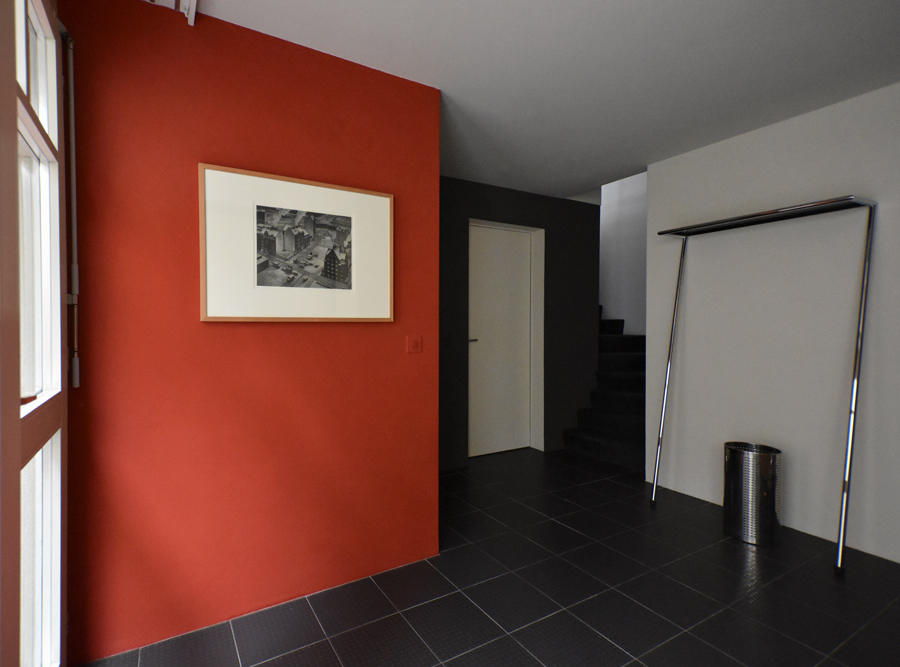 Farbgestaltung + Feng Shui im Innenraum: Das Bild zeigt den Hauseingang im Untergeschoss mit hellem Sandton, Granatrot als bunter Akzent und samtiges Graubraun.