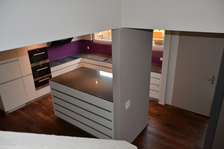 Farbgestaltung Wohnraum: Das Bild zeigt den Blick vom Obergeschoss auf der Treppe zum Hauseingang und zur offenen Küche nach der Renovation.