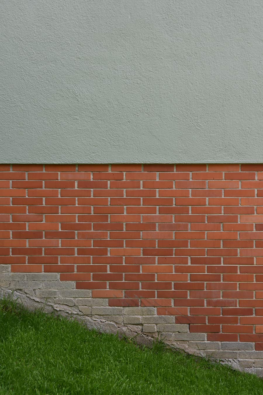 Farbgestaltung Fassade: Das Bild zeigt einen Ausschnitt der Nordostfassade mit dem Zusammenspiel der Farben und Materialien: helles Steingrün im Verputz, roter Backstein und Grün der Natur.