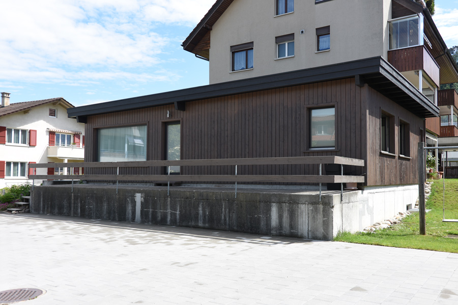 Farbgestaltung Holzfassade: Das Bild zeigt die lange Westfassade mit der Terrasse und die kürzere Südfassade des renovierten Atelieranbaus.
